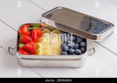 En-cas bleuets, bananes et fraises dans un grand récipient en acier inoxydable. Boîte à lunch sans plastique isolée sur fond blanc. Zéro déchet, écologique. Banque D'Images