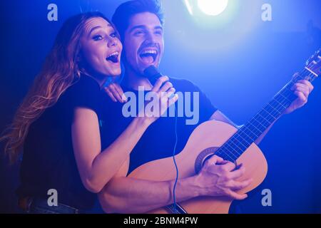 Image de jeunes positifs optimistes amoureux couple musiciens groupe duet sur scène en boîte de nuit sur fond sombre avec des lumières flash. Banque D'Images