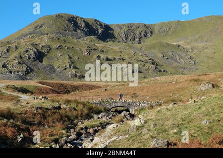 Walker traversant le pont Torver sur la route Wonna SCAR, chemin restreint dans le parc national Lake District, Cumbria, Angleterre Banque D'Images