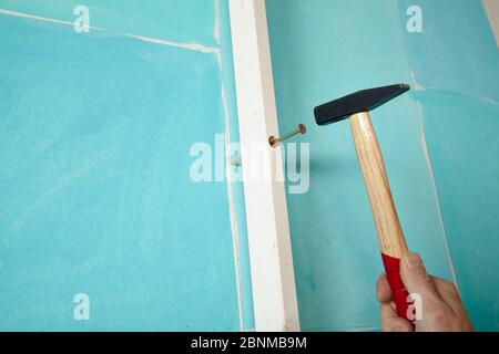 Bricolage mur conception 02, étape par étape faire-il-soi-même production, diverses zones de couleur turquoise séparées par des bandes de bois blanc, étape 09: Marquer les points de perçage dans le mur pour la fixation aux bandes, frapper avec un marteau sur la vis à moitié vissée Banque D'Images