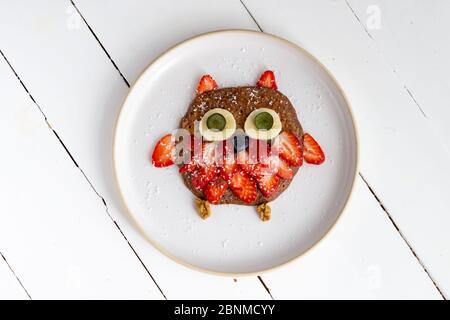 Crêpe hibou créative pour enfants dans une assiette isolée sur fond blanc. Petit déjeuner végétarien sain, déjeuner ou en-cas. Vue de dessus, gros plan Banque D'Images