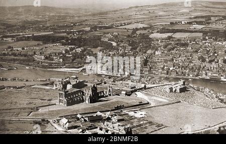 Une ancienne photographie de Whitby (vers les années 1940?) De l'air montrant la ville avant le réaménagement du quai et des zones de cour de charbon de chemin de fer où le magasin Co-op a finalement été construit. On voit aussi le deuxième étang de poissons de l'abbaye de Whitby (en bas à gauche) qui a été rempli. L'érosion des falaises, (à droite) s'était maintenant produite avec une grande partie des champs tombant dans la mer. La croix de la 'marché' sur la plaine de l'abbaye actuelle est vue ici avec le terrain de l'abbaye. Banque D'Images