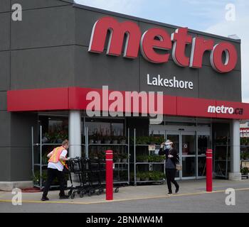 Une femme porte un masque et un masque facial complet pour se protéger du coronavirus à l'extérieur d'une épicerie Metro pendant qu'un employé pousse les chariots dans le magasin. Banque D'Images