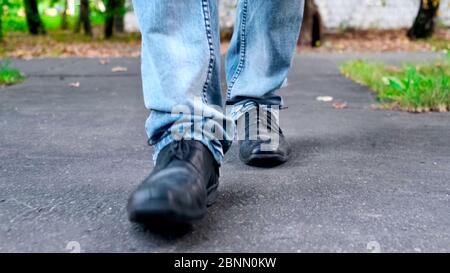 Vue sur les jambes de marche pour homme en jeans bleus et chaussures en cuir noir. Banque D'Images