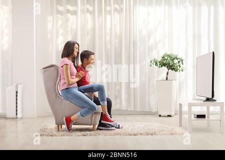 Photo d'un jeune couple assis dans un fauteuil devant un téléviseur à la maison Banque D'Images