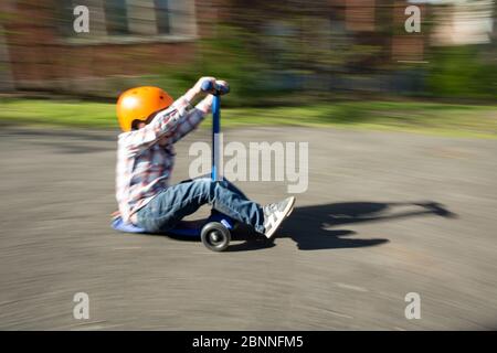 Un garçon extérieur portant un casque orange accélère l'allée sur fond bleu scooter Banque D'Images