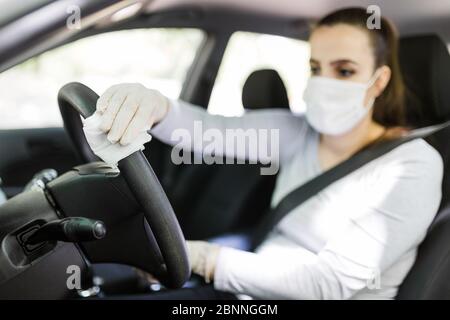 Conducteur féminin utilisant un chiffon humide pour désinfecter le volant de la voiture contre la maladie du coronavirus. Banque D'Images