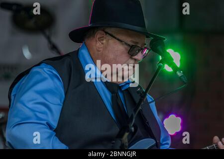 Chanteur senior et guitariste, en concert en plein air, portant un chapeau fedora et des lunettes de soleil. Banque D'Images