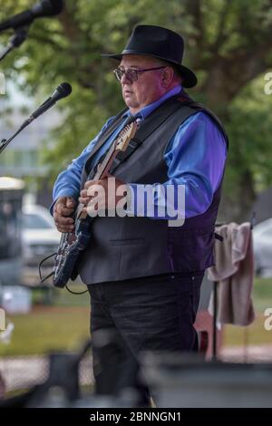 Chanteur senior et guitariste, en concert en plein air, portant un chapeau fedora et des lunettes de soleil. Banque D'Images