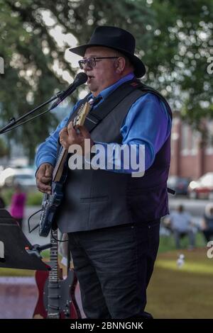 Chanteur senior et guitariste, en concert en plein air, portant un chapeau fedora et des lunettes de soleil. Banque D'Images