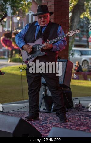 Chanteur senior et guitariste, en concert en plein air, portant un chapeau fedora et des lunettes de soleil. Banque D'Images