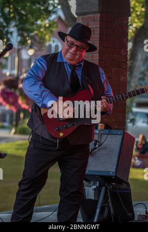 Chanteur senior et guitariste, en concert en plein air, portant un chapeau fedora et des lunettes de soleil. Banque D'Images