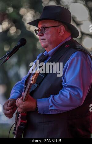 Chanteur senior et guitariste, en concert en plein air, portant un chapeau fedora et des lunettes de soleil. Banque D'Images