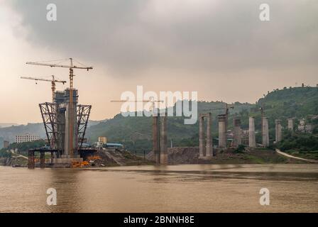 Fengdu, Chongqing, Chine - 8 mai 2010 : fleuve Yangtze. Tours de suspension en béton pour pont en construction avec de hautes grues jaunes sur le wat brun Banque D'Images