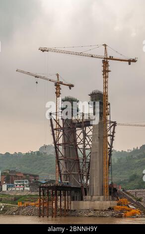 Fengdu, Chongqing, Chine - 8 mai 2010 : fleuve Yangtze. Tour de suspension en béton pour pont en construction avec de hautes grues jaunes sur une manne brune Banque D'Images