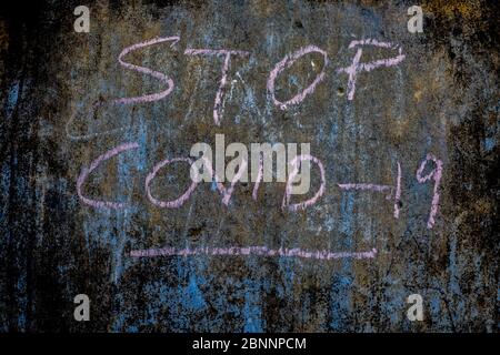 Stop COVID 19 écrit sur un mur de texture rugueuse avec de la craie rose, plan horizontal. Banque D'Images