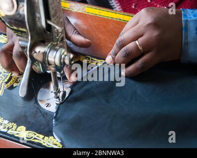 Gros plan de la main d'une femme africaine portant un groupe de mariage, couture sur une machine à coudre. Banque D'Images