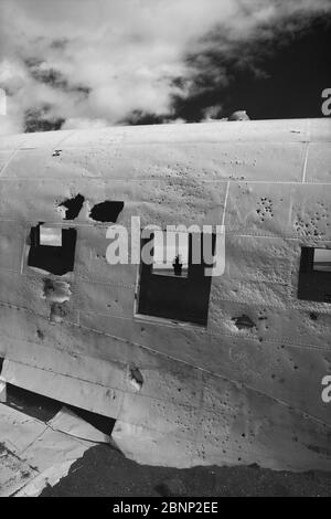 Homme dans une fenêtre d'une épave d'avion DC3 abandonnée sur la plage noire à Sólheimasandur contre ciel sombre Banque D'Images