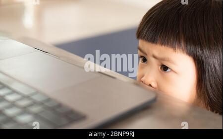 Une fille asiatique regardant un dessin animé effrayant en ligne depuis un ordinateur portable, qui a une expression faciale et une expression lumineuse de peur et d'inquiétude. Banque D'Images