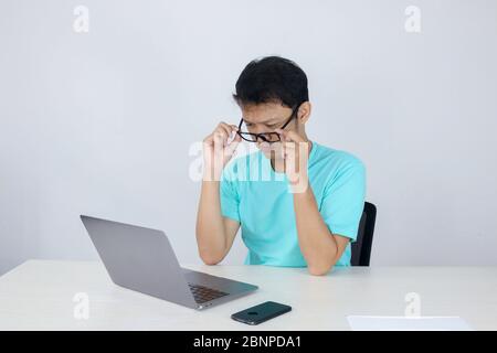 Jeune homme asiatique est sérieux et se concentre sur un ordinateur portable sur la table. Homme indonésien portant une chemise bleue. Banque D'Images