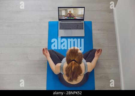 Yoga en ligne. Une fille pratique le yoga en utilisant un ordinateur portable vidéo chat cours assis sur le sol à la maison dans la salle. Vue de dessus. Banque D'Images