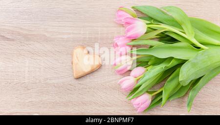 Tulipes roses rouges sur une table en bois clair avec coeur en bois Banque D'Images