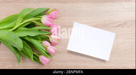 Tulipes roses rouges sur une table en bois clair avec carte postale Banque D'Images