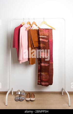 Robes de chambre printemps chemises cuir pantalons chaussures et sandales dans les tons rose-brun sur le cintre et dans les paniers en maille de fil dans la chambre avec un mur blanc Banque D'Images