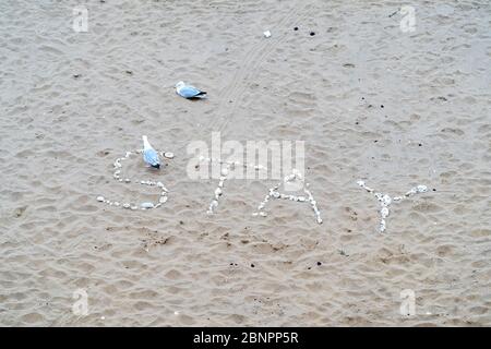 Gros plan du mot « Stay » écrit dans des roches blanches sur le sable de Viking Bay, Broadlairs. Deux mouettes, l'une dans le mot marchant loin, l'autre assise sur le sable au-dessus des pierres. Pendant le verrouillage de COVID-19. Banque D'Images