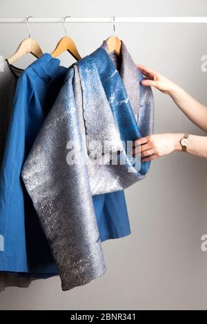 Les mains de jeunes femmes non identifiées atteignent un foulard feutré en soie-laine fait maison, suspendu sur un cintre dans la chambre à côté des vestes bleues sur le gr Banque D'Images