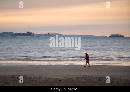 Portland Bill, Dorset, Royaume-Uni. 16 MAI 2020. Météo Royaume-Uni. Un homme descend la plage tôt le matin, au loin trois bateaux de croisière en ancre à weymouth Bay dans Dorset en raison de la fermeture de l'industrie de croisière pendant le confinement du coronavirus. Crédit : DTNews/Alay Live Banque D'Images