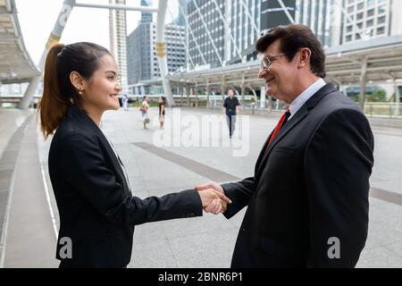 Homme d'affaires mature et jeune femme d'affaires asiatique se serrant la main dans la ville Banque D'Images