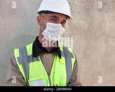 L'ingénieur civil porte un masque médical de protection contre un mur en béton sur le chantier de construction. Banque D'Images