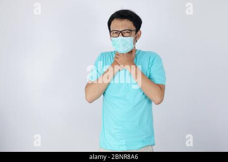 Jeune asiatique ayant mal à la gorge et touchant son cou avec le port d'un masque médical. Banque D'Images