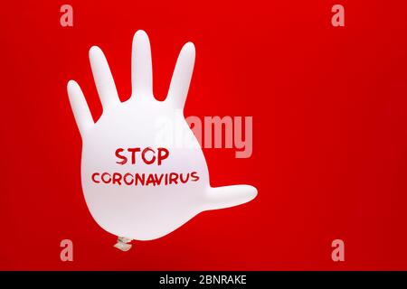 Gant de protection en caoutchouc blanc gonflé avec message texte du virus de la couronne d'arrêt sur fond rouge avec espace de copie. Banque D'Images
