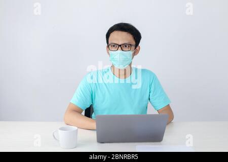 Jeune homme asiatique en t-shirt bleu avec un travail sérieux avec l'ordinateur portable sur la table et regardant à l'extérieur Banque D'Images