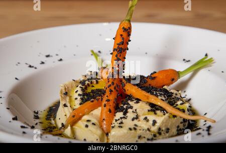 Gros plan d'une assiette de houmous avec de la poudre d'olive noire, de l'huile d'olive et des carottes sur fond de bois. Image isolée Banque D'Images