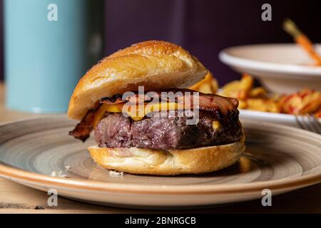 Hamburger rustique au bœuf avec fromage et bacon servi sur une assiette. Banque D'Images