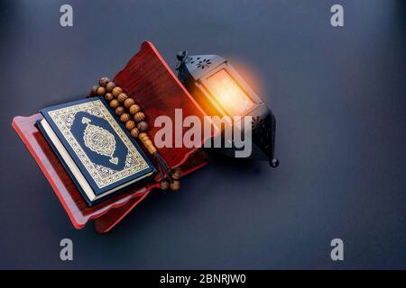 Saint Al Quran avec la calligraphie arabe écrite signification d'Al Quran, lampe de lanterne et perles rosaires ou tasbih sur fond noir. Banque D'Images