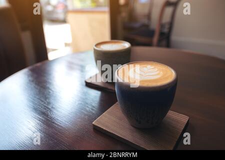 Gros plan de deux petites tasses de café au lait chaud avec art au lait sur une table en bois vintage dans le café Banque D'Images