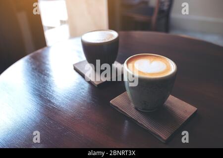 Gros plan de deux petites tasses de café au lait chaud avec art au lait sur une table en bois vintage dans le café Banque D'Images