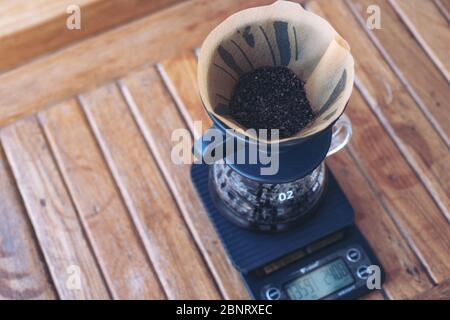 Image en gros plan de la mouture de café dans un filtre en papier sur une balance numérique tout en faisant un café goutte à goutte sur une table en bois vintage Banque D'Images