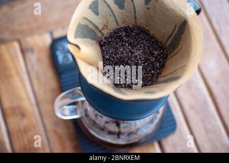 Image en gros plan de la mouture de café dans un filtre en papier sur une balance numérique tout en faisant un café goutte à goutte sur une table en bois vintage Banque D'Images