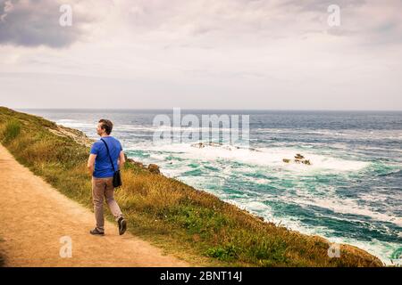 homme en chemise bleue marchant au bord de la mer sur une route de terre Banque D'Images