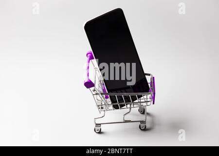 Vue de dessus d'un smartphone dans un chariot Mini Shopping sur une surface blanche Banque D'Images