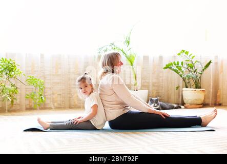 Femme mature et petite fille assise sur un tapis dans lotus poser et méditer tout en faisant du yoga dans la chambre spacieuse à la maison ensemble Banque D'Images