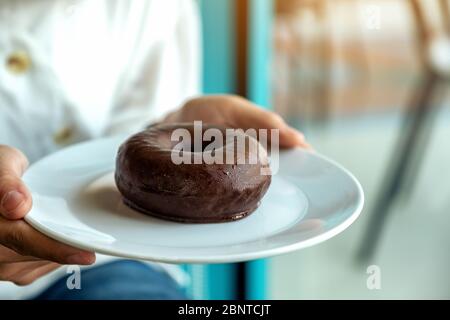 Une femme tenant et montrant une assiette de beignet de chocolat Banque D'Images
