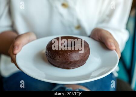 Une femme tenant et montrant une assiette de beignet de chocolat Banque D'Images