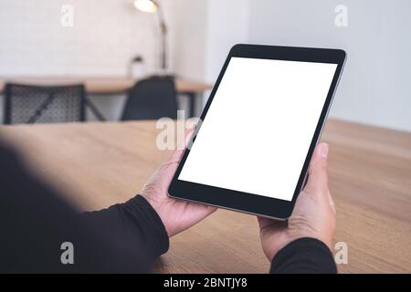 Image de maquette d'un PC tablette noir avec écran blanc vierge pendant qu'il est assis au bureau Banque D'Images