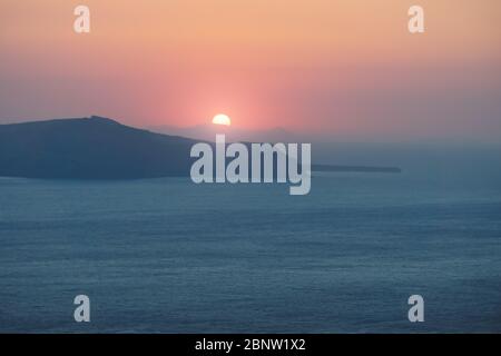 Coucher de soleil derrière les îles avec des lumières rouges violettes sur l'océan bleu aux falaises de Fira, Santorini, Grèce Banque D'Images